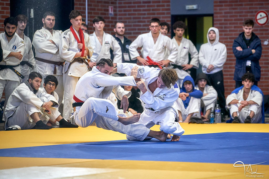 Deux judokas en plein combat, pendant que d'autres judokas regardent